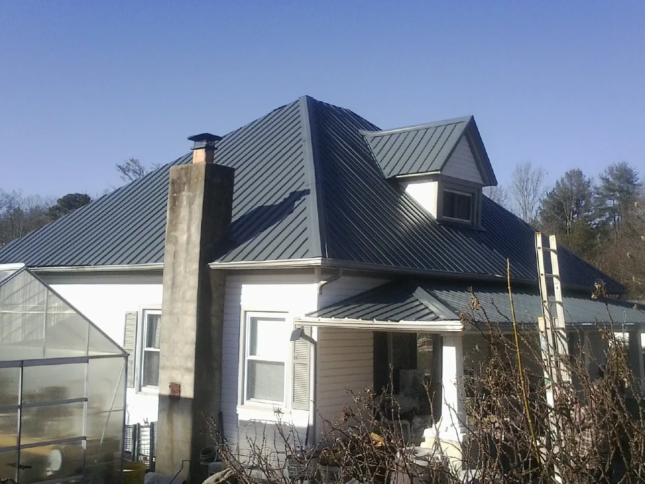 Dark blue standing seam metal roof on a white farmhouse with dormer — Slate & Tile Roof Repair by Roofing Brothers in Bentonville