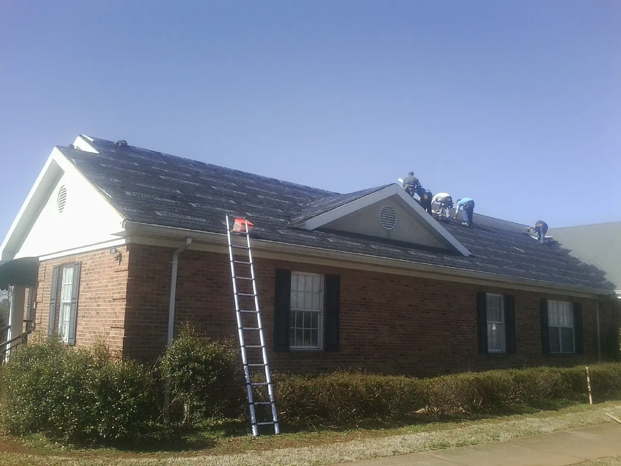 Crew tearing shingles off a brick ranch roof with a ladder set — Metal Roof Repair work by our crew in Bentonville