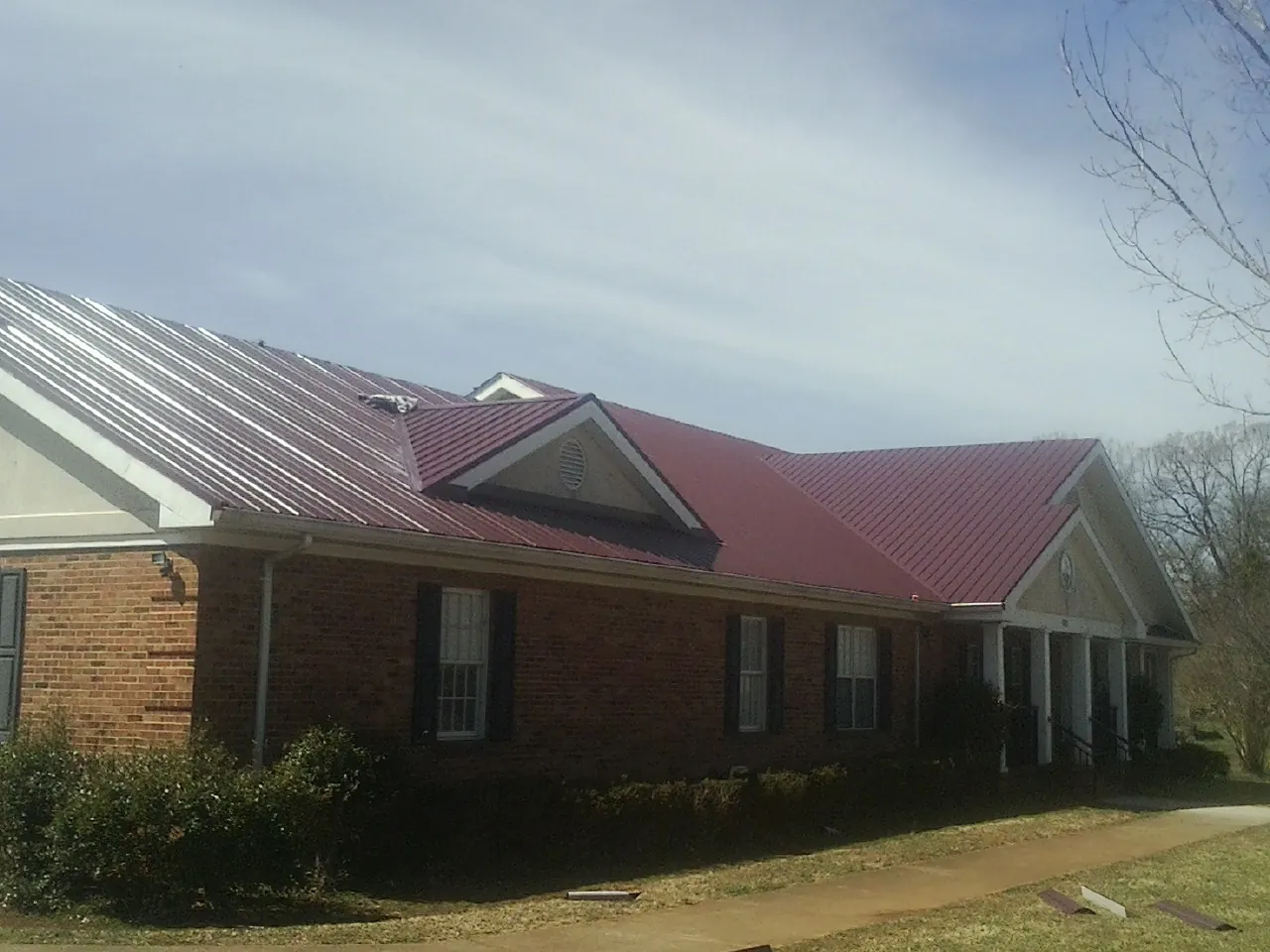 Red metal roof with gabled entries on a long brick building, from a Hail Damage Roof Repair job in Bentonville
