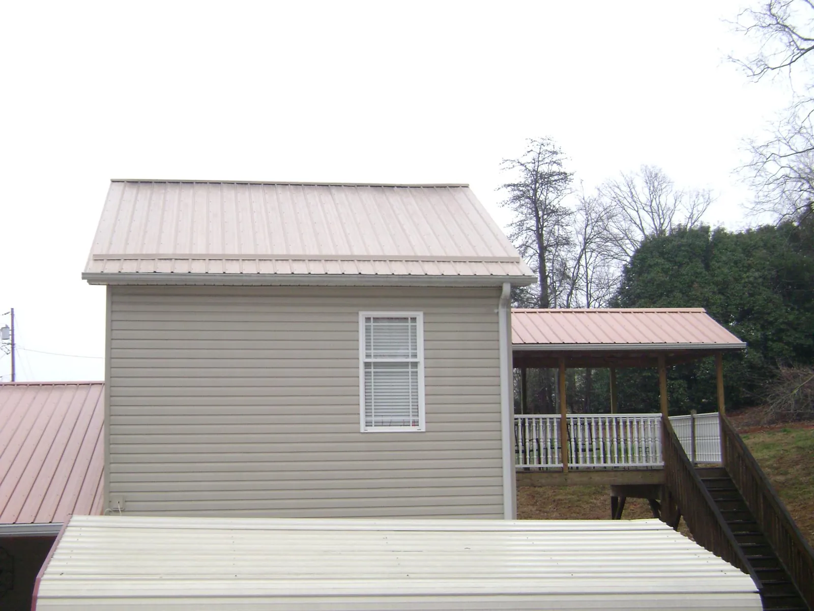 Tan metal roofs on a two story addition and attached porch, from a Roof Replacement job in Bentonville