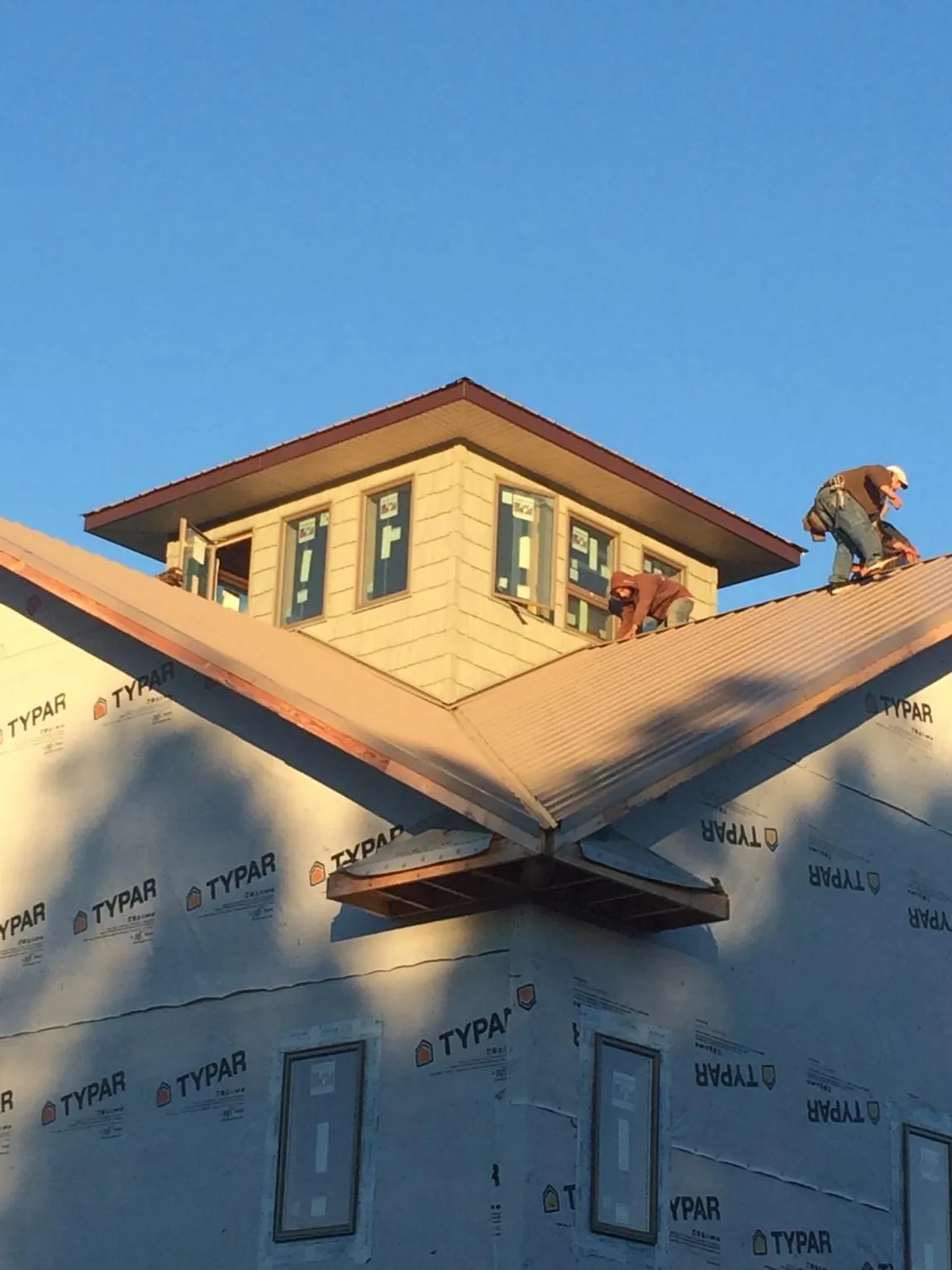 Roofers working around a rooftop cupola on a new metal roof at sunset — Roof Waterproofing in Bentonville by Roofing Brothers